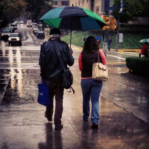 old man carrying an umbrealla for a girl and walking in the rain