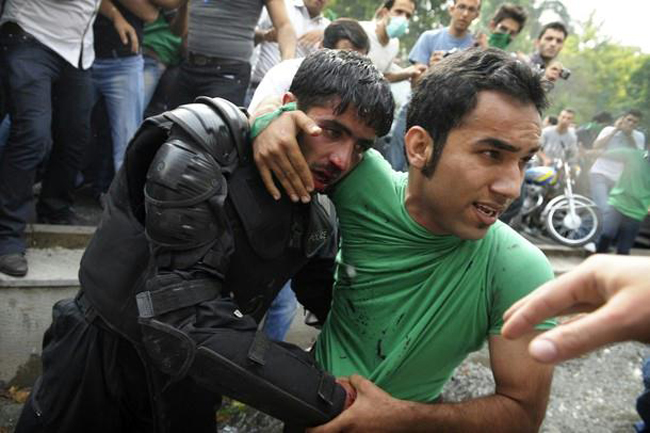 An Iranian police officer is protected by civilians after being beaten by rioters [Tehran, Iran, 2009]