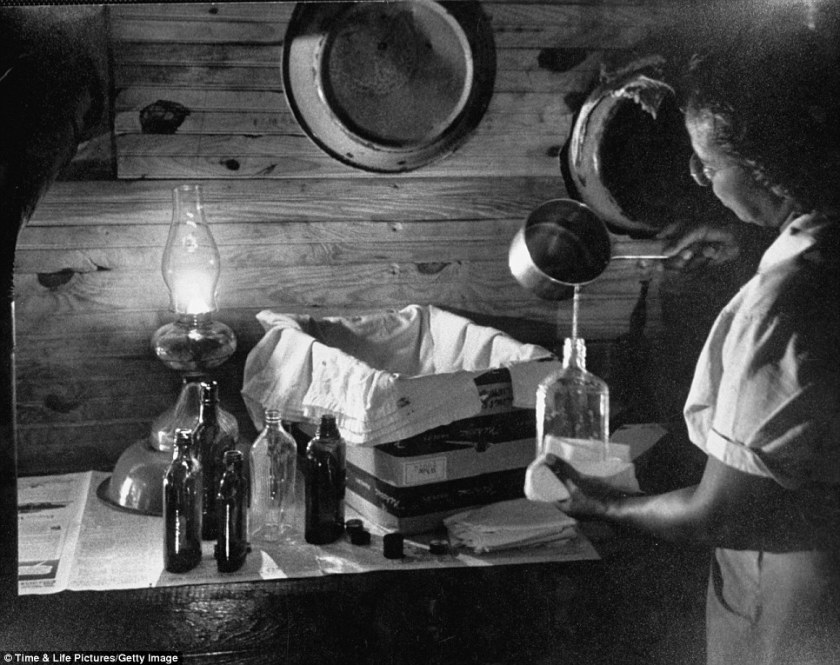 Maude Callen preparing a solution in front of an incubator made from a box and whiskey bottles full of warm waterRead more