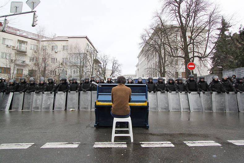 Man sits playing piano to riot police. Ukraine – December 2013
