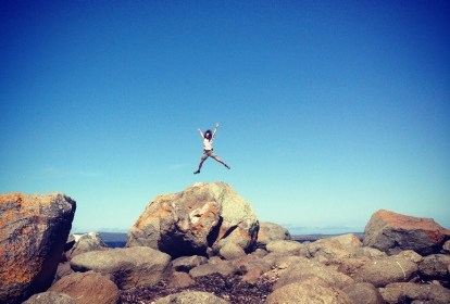 Woman jumping in air from large rock at the beach