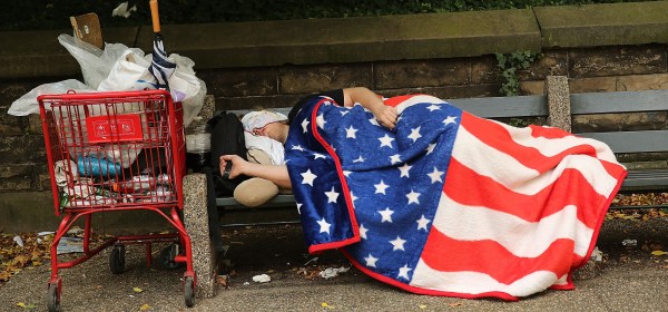 A homeless man sleeps under an American flag blanket