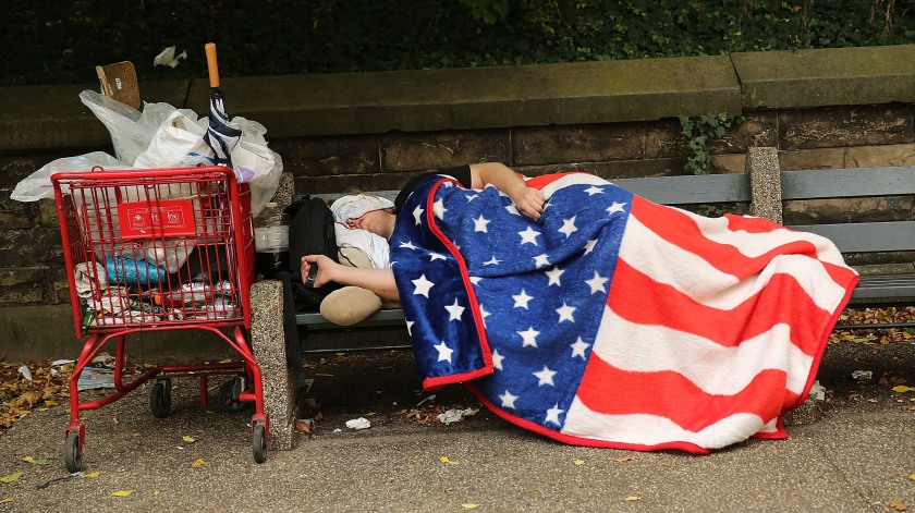 A homeless man sleeps under an American flag blanket